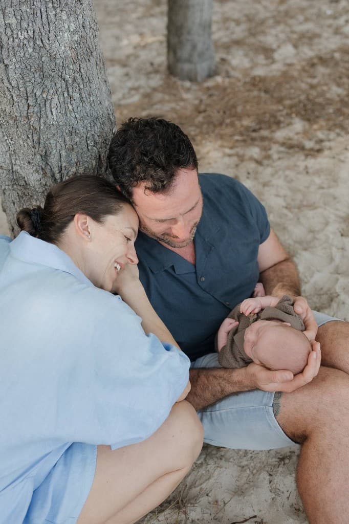 Kate and Greg, the founders of Healthly, sitting under a tree with their baby
