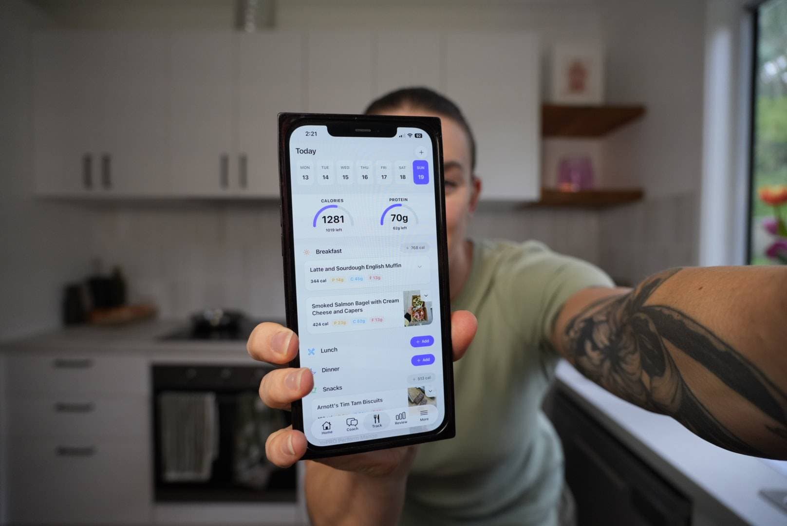 Kate holding a phone displaying the Healthly app in her kitchen
